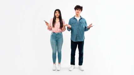 Displeased Young Couple Using Mobile Phones Standing Over White Background