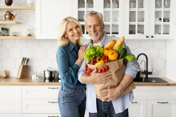 Happy senior couple posing with grocery bag in kitchen interior