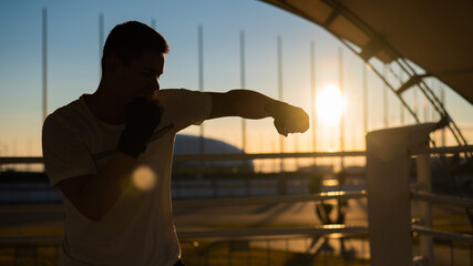 A man trains in boxing at the stadium at sunset. Athlete silhouette.