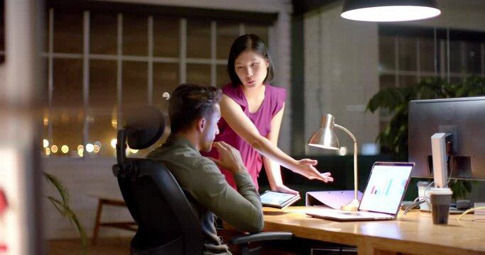 Focused diverse male and female colleague discussing work using tablet and laptop at night in office