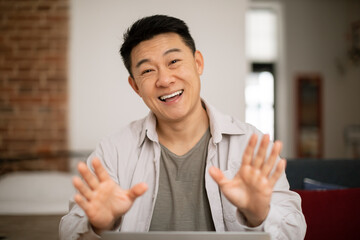 Cheerful korean man having virtual online meeting and emotional conversation, gesturing to camera,...