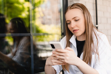 Charming serious woman reading news on mobile phone during rest in coffee shop. Concept: using the phone. Mobile phone print sms or browser online. Concentrated girl, scroll social media, messaging.