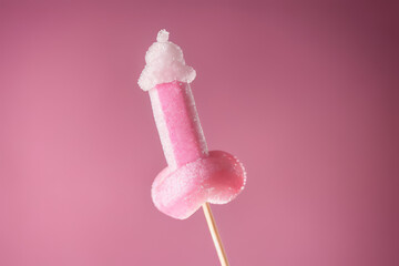 Pink sugary lollipop in form of penis on stick on a pink plain background - obrazy, fototapety, plakaty