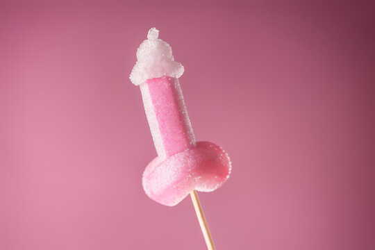 Pink sugary lollipop in form of penis on stick on a pink plain background