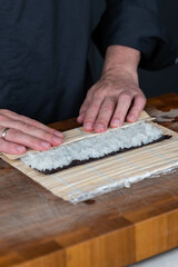 Close up of sushi chef hands preparing japanese food. Man cooking and making rice for sushi at restaurant. Traditional asian seafood rolls on cutting board.