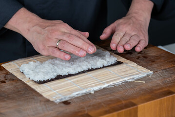 Close up of sushi chef hands preparing japanese food. Man cooking and making rice for sushi at restaurant. Traditional asian seafood rolls on cutting board.