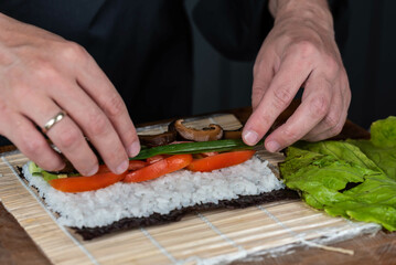 Close up of sushi chef hands preparing japanese food. Man cooking sushi at restaurant. Traditional asian seafood rolls on cutting board.