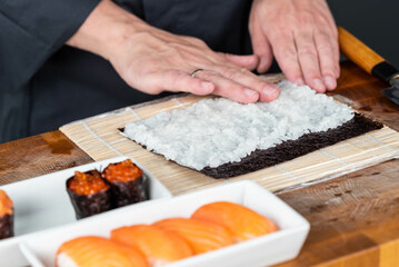Obraz na płótnie Canvas Close up of sushi chef hands preparing japanese food. Man cooking sushi with red caviar and salmon at restaurant. Traditional asian seafood rolls on cutting board.