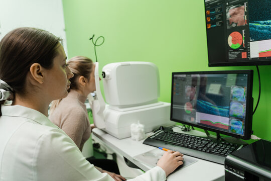 Examination of eyes of patient using optical coherence tomograph. Optical coherence tomography OCT scan to create pictures of the back of eye. Ophthalmologist is scanning cornea of woman patient.