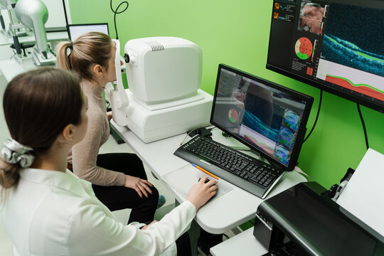 Examination of eyes of patient using optical coherence tomograph. Optical coherence tomography OCT scan to create pictures of the back of eye. Ophthalmologist is scanning cornea of woman patient.