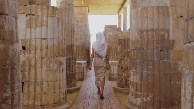 Woman is walking amongst world's oldest known stone columns at Djoser's step pyramid complex.