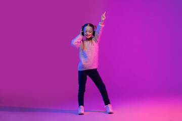 Joyful school aged girl with headphones dancing in neon light