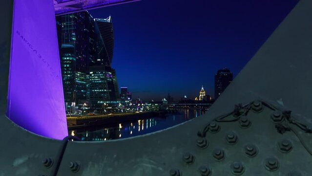 Moscow river near the skyscrapers of Moscow City district in the night timelapse hyperlapse view under the bridge between supports. Reflection on water, illuminated buildings