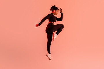 Fototapeta na wymiar Dynamic moves. Determined black lady exercising, doing elbow to knee crunches or jumping on red neon background