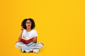 Happy shocked curly teen african american girl in white t-shirt, glasses, reading book, got idea