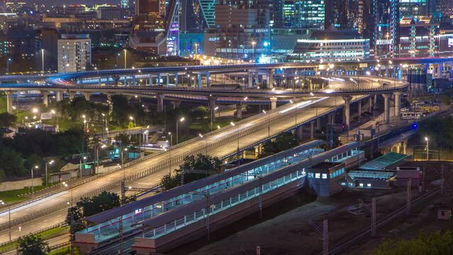 Small Ring of the Moscow Railways night timelapse. Orbital railway route in Moscow, Russia. Shelepikha Station aerial top view with traffic on third transport ring and skyscrapers behind