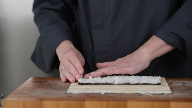 Close up of sushi chef hands preparing japanese food. Man cooking and making rice for sushi at restaurant. Traditional asian seafood rolls on cutting board.
