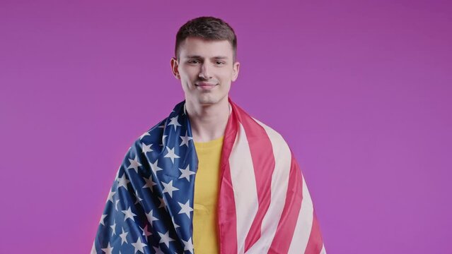 Happy young man with national USA flag on pink background. American patriot