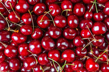 Red sweet cherries background. Pile of fresh red ripe sweet cherry with stalk. Food, berry background, backdrop, wallpaper. Top view, flat lay.
