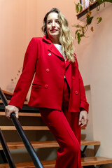 Stylish woman in red suit posing standing on stairs.
