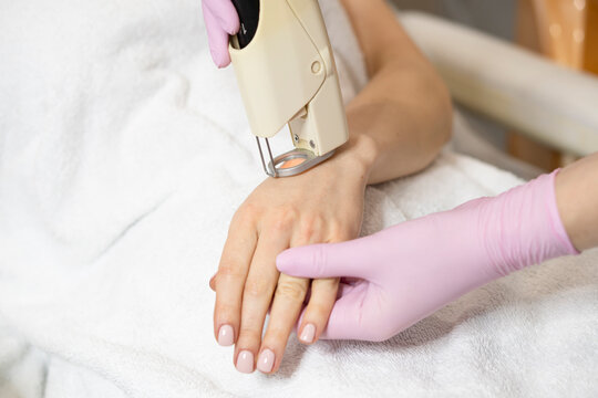 A beautiful female client undergoes a laser hair removal procedure on her fingers in a beauty salon. skin and body care concept with new technologies.