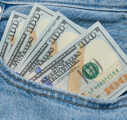Paper American dollar bills protrude from the back pocket of blue jeans