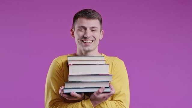 Young male student holds stack university books from college library on pink