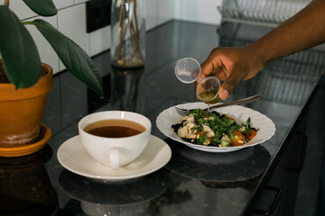Close up african american man cooking salad and pouring olive oil - dinner or lunch concept