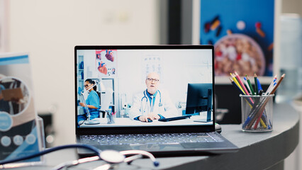 Medic using online videocall at desk, laptop placed on hospital registration counter with...