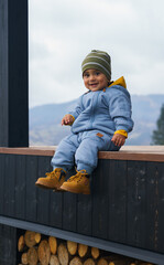 Adorable baby boy in warm clothes sitting on terrace outdoors