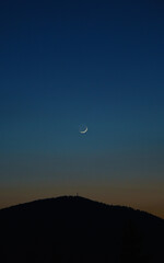 Young moon above mountain peak on blue sky