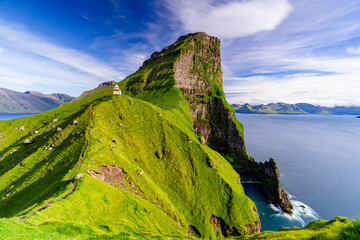 Kallur lighthouse on cliffs covered with grass with Borgarin mountain peak on background, Kalsoy island, Faroe Islands, Denmark, Europe