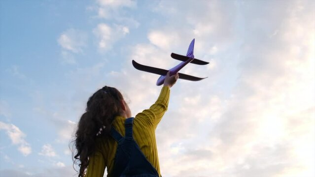 Happy little girl child with toy airplane at sunset summer nature. Concept success leader winner, travel freedom. Cute female kid dreams of becoming an airline pilot. Children's dream to run with toy