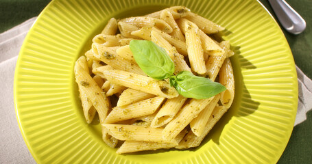 Penne Pasta with Pesto Sauce. green background. traditional Italian dish. camera movement at an angle. frame close ap.