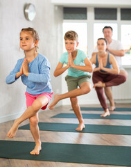 Fototapeta na wymiar Family with two children doing yoga on mats in fitness studio..