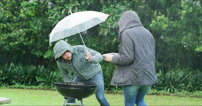 Protection, couple with an umbrella for life insurance and cover in backyard with rain. Security or safety, funny disaster and people with raining equipment for cover with food at their home or house