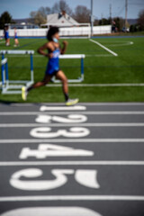 Defocused abstract vertical background image of a young runner racing on numbered lane athletic track with copy space. Shot in natural light.