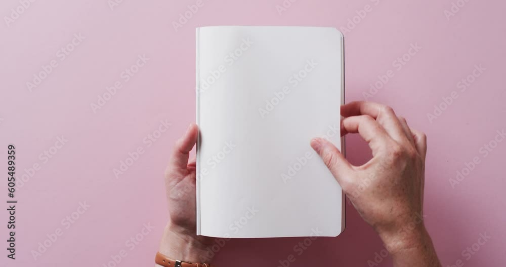 Poster Close up of hand leafing through book with copy space on pink background in slow motion