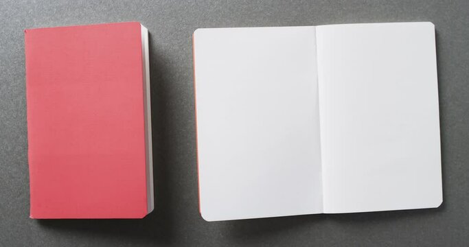 Close up of open blank book and pink book with copy space on gray background in slow motion
