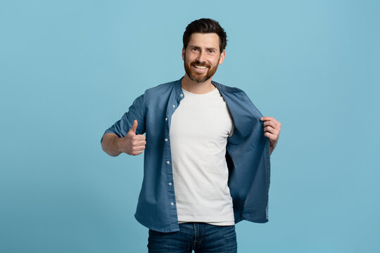 Handsome bearded man in casual denim and white mockup t-shirt, humbs up at camera, isolated on bue