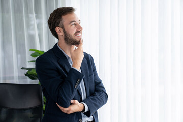 Handsome businessman in black suit stand confidently in his modern office portrait, deep in thought...