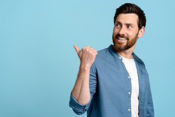 Studio portrait smiling handsome bearded pointing aside at copy ad space on isolated blue background