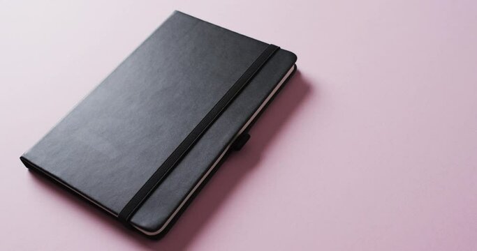 Close up of closed black notebook with copy space on pink background in slow motion
