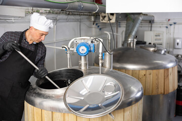 Brewer is controls the brewing process near reservoir with beer indoor.