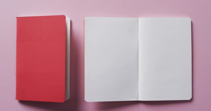 Close up of open blank book and red closed book with copy space on pink background in slow motion