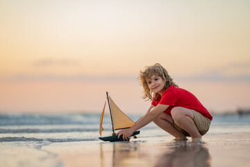 Little blonde boy put toy boat in the sea waves at the beach during summer vacation. Childhood and...
