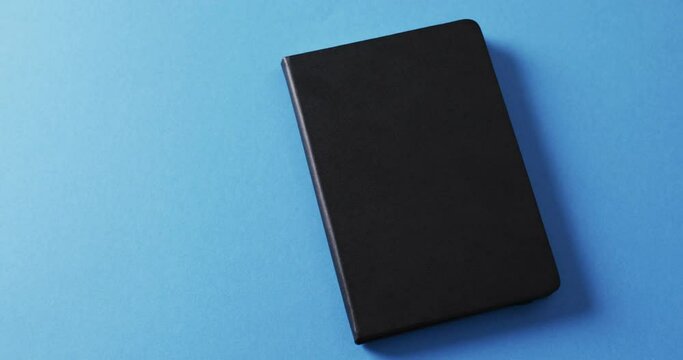 Close up of closed black book with copy space on blue background in slow motion