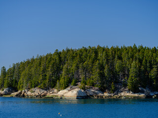 The rocky shoreline and deep forest along the bay front on Vinalhaven Island Maine on a beautiful spring blue sky day