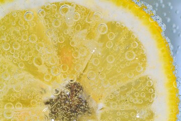 Slice of ripe lemon in water. Close-up of lemon in liquid with bubbles. Slice of ripe citron in...