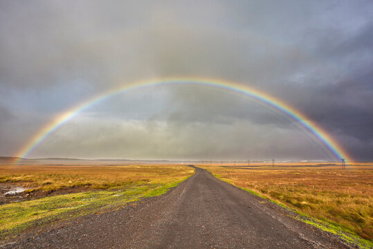 A rainbow straddles a road in countryside near Rif, Snaefellsnes peninsula, western Iceland, Polar Regions